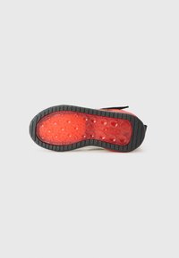 Semelle en caoutchouc de basket avec une surface rouge texturée présentant des motifs circulaires en relief, entourée d'un bord noir pour l'adhérence.