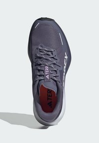 Zapatilla de running para hombre en malla gris oscuro con acentos morados. Cuenta con un cierre de cordones, superficie texturizada y suela acolchada.