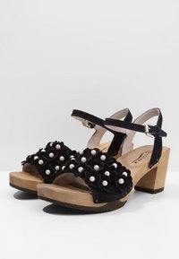 Sandali open-toe neri in suede con decorazioni floreali arricchite da perle bianche, tacco in legno chunky e cinturino alla caviglia con chiusura a fibbia.
