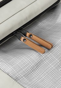 Interno di una borsa in tela grigia con due cerniere nere dotate di manici in pelle marrone su un fodero a motivo a griglia. Texture liscia con accenti a contrasto.