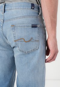 Light blue denim jeans featuring a classic design, with a pocket accentuated by orange stitching and a small blue tag on the waistband.