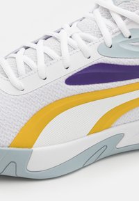 Chaussure de course avec une tige blanche texturée, des accents jaunes et violets, et une semelle extérieure bleu clair. Les lacets sont blancs et le design est élégant.