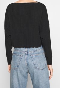Black cropped long-sleeve top with a ribbed texture and scalloped hem, paired with high-waisted light blue denim jeans featuring back pockets.