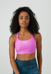 Rosa Sport-BH mit Racerback-Design und weißem Logo, aus dehnbarem Stoff. Kombiniert mit türkisfarbenen, gemusterten Sportshorts.
