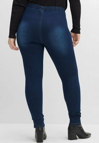Mörkblå stretchiga leggings med elastisk midja, åtsittande design och slät denimliknande textur. Svarta ankelstövlar passar till.