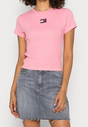 Kobieta ubrana w dopasowany, różowy, krótkotrwały t-shirt Tommy Jeans oraz szarą jeansową spódnicę z wysokim stanem i postrzępionym brzegiem.