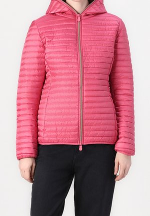 Persoon draagt een felroze doorgestikte jas met ritssluiting en kap, met lange mouwen en zwarte broek, tegen een effen witte achtergrond.