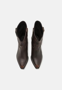 Bottines en cuir marron avec un bout pointu, des coutures minimales et un talon bas. Elles disposent de languettes pour un enfilage facile. Texture lisse.