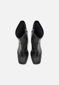 Une paire de bottines en cuir noir avec des bouts carrés et des fermetures éclair sur les côtés, vues du dessus sur un fond blanc.