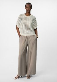 Roomwitte gebreide top met brede mouwen, gecombineerd met losse beige broek. De outfit heeft zachte texturen en een ontspannen silhouet.