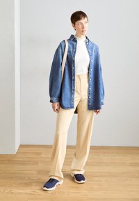 Jeanshemd mit entspannter Passform, weißem Rollkragenpullover, beigen weit geschnittenen Hosen und navy Sneakern. Enthält eine neutrale Schultertasche.