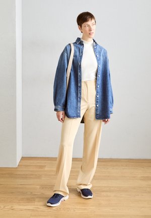 Camisa de denim de corte relajado, suéter blanco de cuello alto, pantalones beiges de pierna ancha y zapatillas de deporte azul marino. Incluye un bolso de hombro neutro.