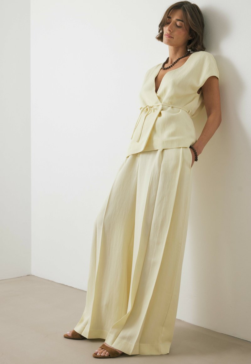 Ensemble deux pièces jaune clair comprenant un haut croisé avec un détail noué et un pantalon à jambe large, fabriqué à partir d'un tissu doux et fluide avec une texture lisse.