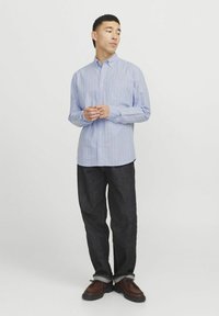 Camicia a righe blu chiaro con bottoni, maniche lunghe, colletto e una tasca sul petto, abbinata a jeans denim scuri e scarpe marroni.