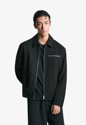 Svart zip-up jacka med krage och en framficka som har en silverdragkedja. Tillverkad av en slät tyg med en avslappnad passform och långa ärmar.