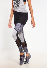 Leggings neri e grigi a motivi con pannelli in rete, caratterizzati da un design in pelle di serpente sulle gambe inferiori. Abbinati a sneakers grigie.
