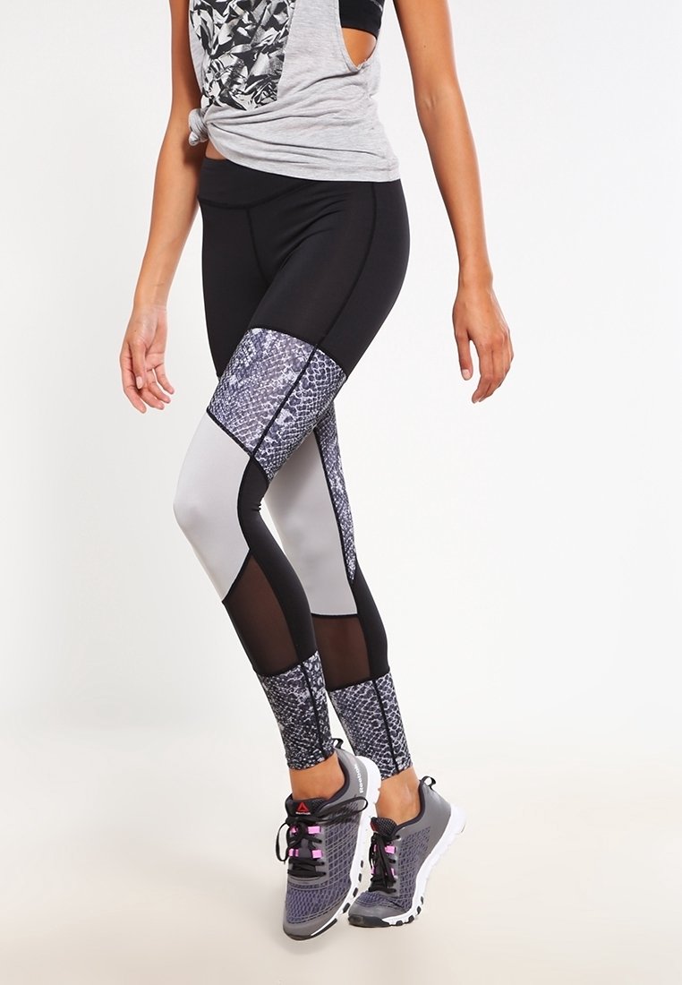 Leggings neri e grigi a motivi con pannelli in rete, caratterizzati da un design in pelle di serpente sulle gambe inferiori. Abbinati a sneakers grigie.