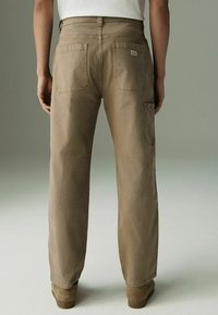 Pantalons en coton beige avec une coupe droite, dotés de deux poches arrière et d'une poche latérale, présentés sur un fond neutre.