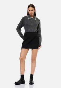 Grijze gebreide trui met een met parels beklede kraag, gecombineerd met een zwart minirok met hoge taille en zwarte schoenen met een chunky zool.