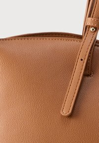 Sac à main en cuir marron avec une surface texturée, doté d'une bandoulière lisse et de coutures contrastantes. Accent sur des lignes épurées et un design minimaliste.