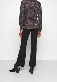 Zwarte flarebroeken gecombineerd met een blouse met een donker patroon, voorzien van een ronde hals en lange mouwen. Model draagt zwarte enkellaarsjes met een hak.