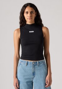 Crni bezrukavni kratki top s visokim ovratnikom, na kojem se nalazi bijeli natpis "LEVI'S" sprijeda; model uparen sa svijetloplavim trapericama visokog struka.