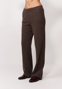 Brązowe dresowe spodnie wykonane z dzianiny o luźnym kroju, z elastycznym paskiem w talii, bocznymi kieszeniami oraz gładką teksturą sięgającą do ziemi.
