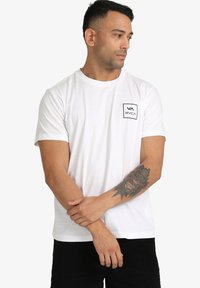 T-shirt en coton blanc à manches courtes et col rond. Présente un petit logo rectangulaire noir sur la poitrine gauche.