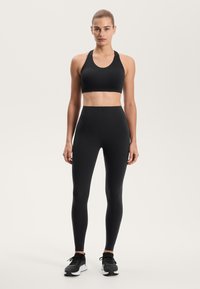 Czarny zestaw sportowy składający się z dopasowanego biustonosza sportowego z wycięciem w kształcie litery U oraz legginsów z wysokim stanem. Oba elementy mają gładką, elastyczną fakturę.