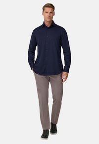 Námornícka dlhá košeľa s gombíkmi v kombinácii so svetlo šedými nohavicami a čiernymi teniskami. Košeľa má klasický golier a hladkú textúru.