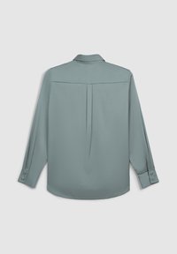Camicia a maniche lunghe in morbido tessuto blu chiaro con piega sul retro. Presenta un colletto a punta e polsini con bottoni per la chiusura.
