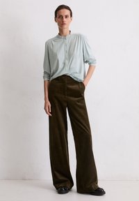 Camicia azzurro chiaro a maniche lunghe con bottoni e spalle a pieghe, abbinata a pantaloni larghi in velluto a coste verde oliva e scarpe nere basse.