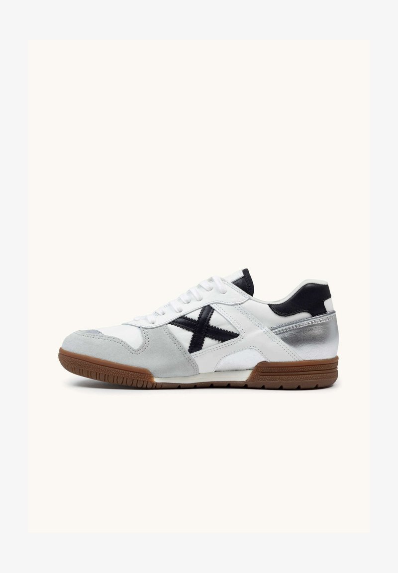 Baskets basses blanches avec des accents gris, logo noir "X" sur le côté, détail talon noir, lacets blancs et semelle en caoutchouc marron.
