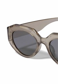 Gafas de sol de ojo de gato en plástico gris translúcido con lentes oscuros. Presentan un marco esculpido y una textura suave, que realzan el diseño moderno.