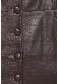 Ciemnobrązowa skóra krokodyla z faux z dopasowanymi, teksturowanymi guzikami i szczegółowym przeszyciem na odzieży.