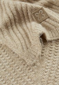 Beige wollen gebreide stof met ribbeltextuur en een opgenaaide patch met een eenvoudig klavertrek in bijpassende beige tinten.