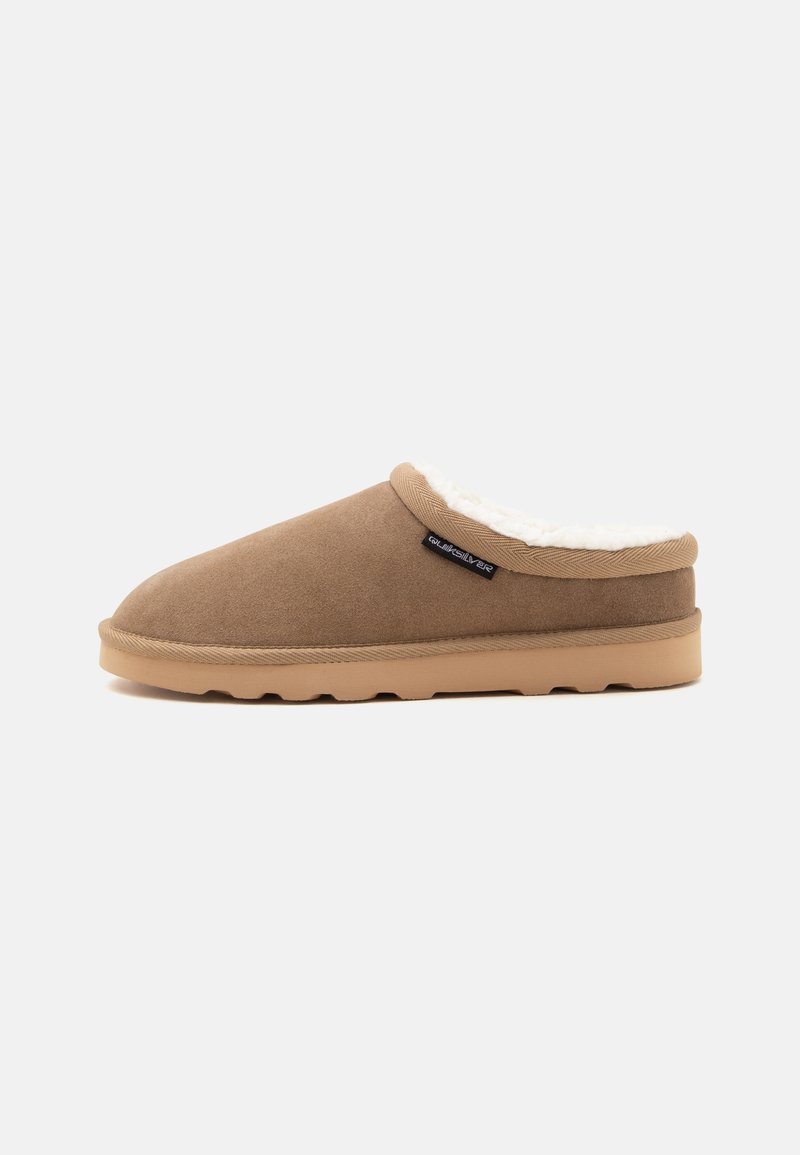 Καφέ παντόφλα τύπου slip-on με μπεζ σόλα και λευκή χνουδωτή επένδυση, πλαϊνή ετικέτα με το λογότυπο Quiksilver, εμφανίζεται σε προφίλ πάνω σε απλό φόντο.