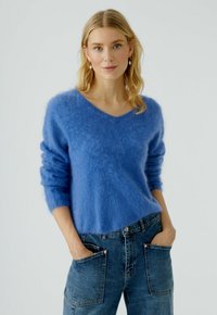 Blaues, flauschiges Mohair-Mischpullover mit V-Ausschnitt und langen �Ärmeln, kombiniert mit lockeren blauen Jeans aus Denim mit großen aufgesetzten Taschen.