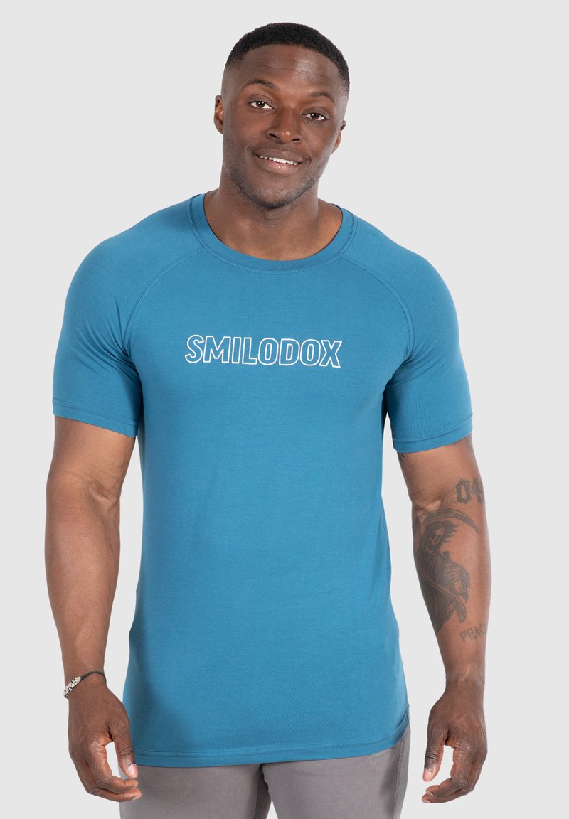 Tyrkysové sportovní tričko s krátkými rukávy a kulatým výstřihem. Na přední straně se nachází bílé logo "SMILODOX". Měkká, hladká látka.