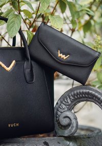 Black textured handbag and matching wallet with gold decorative accents. Handbag features two handles and a logo, while wallet has a flap closure.