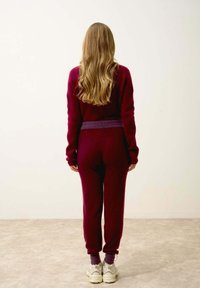 Bordowy sweter i pasujące joggery o teksturowanym splotach, z fioletowym pasem w talii. Model nosi jasne trampki.