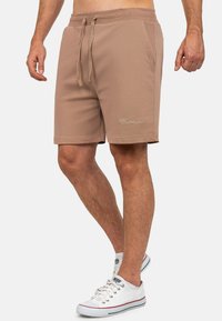 Pantaloni sportivi marroni con tessuto testurizzato, vita elastica, cordino e tasche laterali; presenta un logo ricamato sulla gamba.
