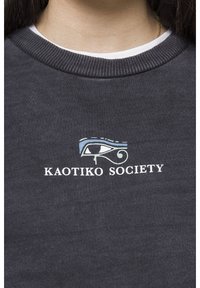 Šedá mikina s kulatým výstřihem. Na hrudi je nápis „KAOTIKO SOCIETY“ doplněný stylizovaným motivem oka v modré a zelené barvě.