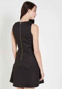 Vestido negro sin mangas con patrón de rosas texturizado, corsé ajustado, falda acampanada y una cremallera dorada en la parte trasera.