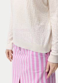 Ljus, texturerad krämfärgad tröja med ribbad fåll, kombinerad med en rosa randig kjol med blå och vita vertikala linjer och sidodel.