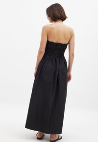 Robe maxi noire sans bretelles avec un corsage smocké et une jupe fluide. Fabriquée en tissu léger avec une texture lisse.
