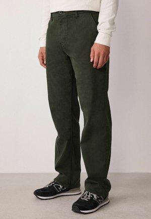Olivgrüne gerade geschnittene Hose aus weichem Stoff mit Knopf an der Taille, kombiniert mit schwarzen Sportschuhen.