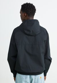 Chaqueta negra con capucha, de exterior liso, puños elásticos y dobladillo acanalado. La parte trasera presenta un diseño limpio, sin logotipos ni patrones visibles.
