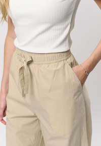 Beiget puuvillasekoitehousut, joissa on joustava vyötärönauha, edessä solmittava yksityiskohta ja sivutaskut; sileä pinta, jossa hienoinen kiilto.