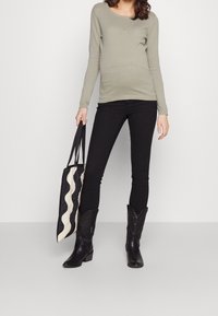 Haut à manches longues texturé kaki assorti à un jean noir ajusté et des bottes de cow-boy noires. Le sac présente un motif ondulé en noir et crème.